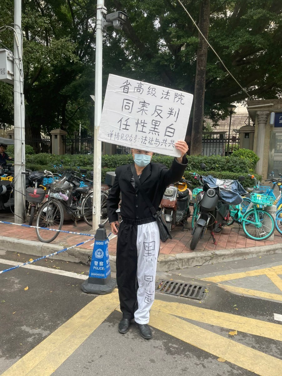 2025年12月25日，广东省广州市天河区广东省高级人民法院门前，一名男子身穿讽刺法院“半黑半白、黑白颠倒”的裤子，手举标语牌控诉省高级法院，称其“同案反判，任性黑白”。
