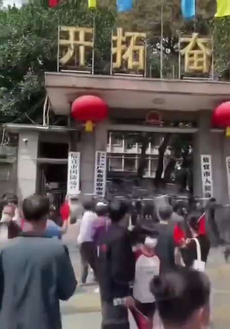 3月19日，信宜市政府门口前，部分维权群众向在场的防暴警察投掷杂物。当一名群众被控制并遭到殴打时，周围数十名群众迅速上前，将其解救出来。混乱之中，信宜市人民政府门口的标识牌一度被拉扯松动，在风中摇晃，...